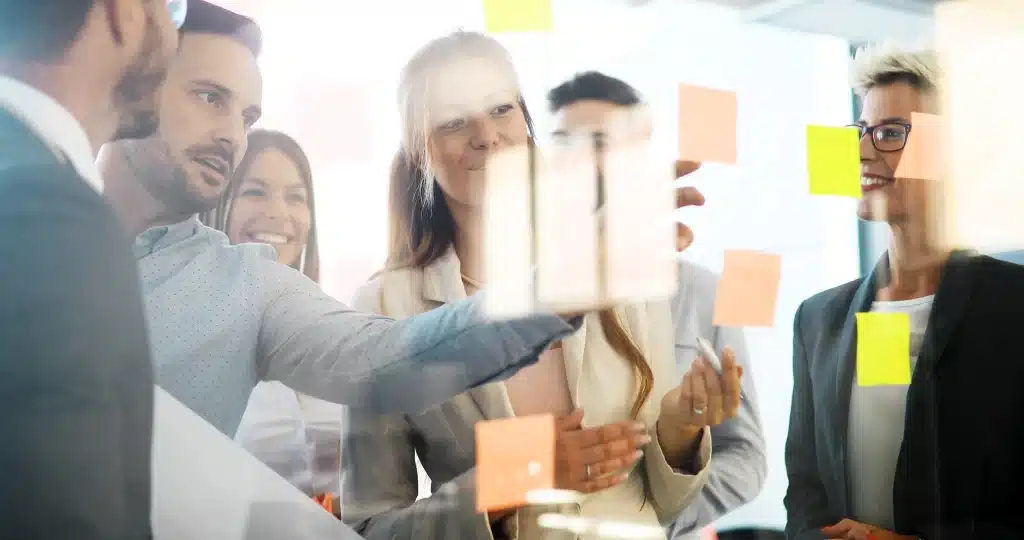 3 hommes et 3 femmes debout en formation et qui placent des post-it sur un mur transparent