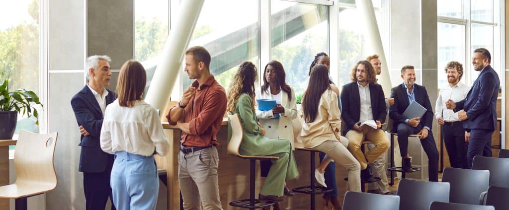 12 professionnels discutent en petits groupes de 2 ou 3 personnes lors d'une formation inter-entreprise.