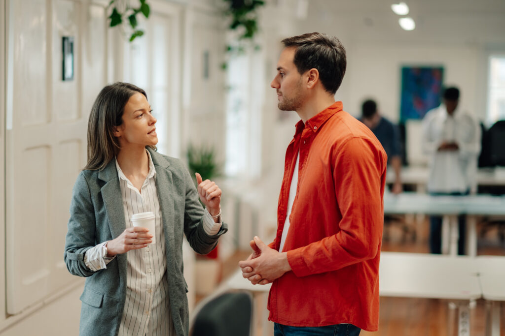 businesswoman holding coffee cup talking to businessman in office hallway