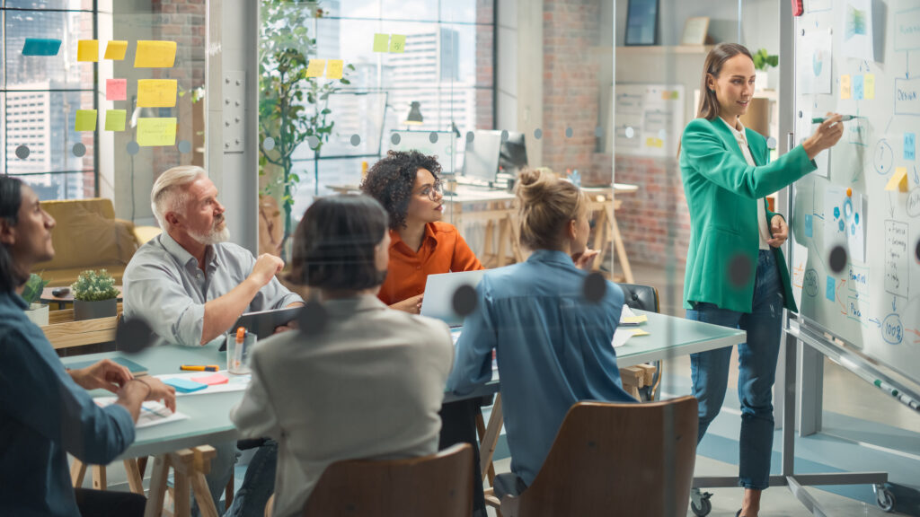 motivated group having a meeting in the office conference room. female project manager explaining growth strategy to diverse team of investors using whiteboard to show charts and statistics